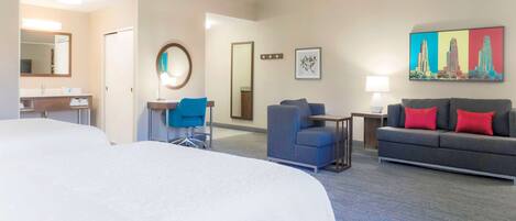 A hotel room with a large bed, a desk with a chair, a sofa with red cushions, and a painting on the wall.