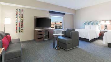 Ein Hotelzimmer mit Bett, Fernseher, Sofa, kleinem Tisch und einem Fenster mit Blick.