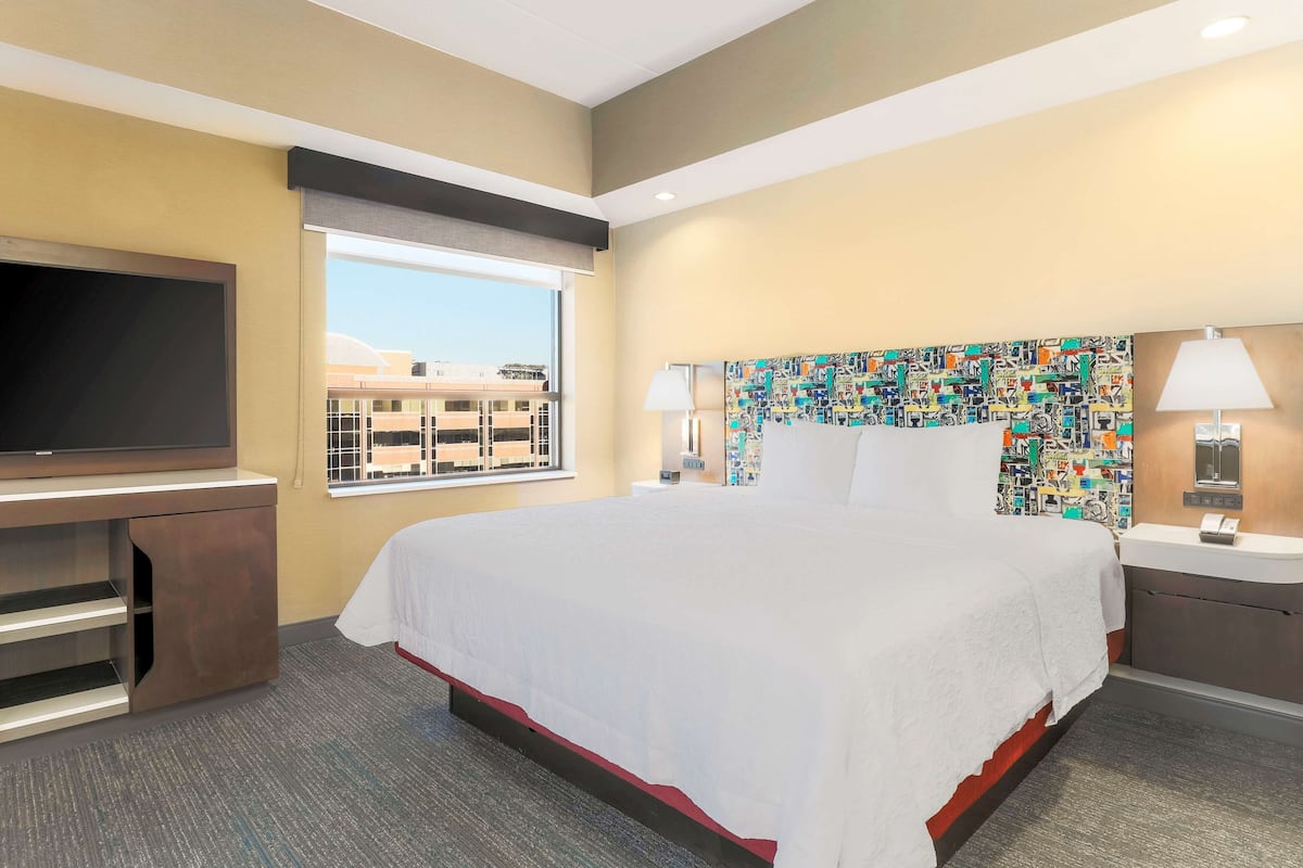Quarto de hotel com uma cama grande, televisão de tela plana, escrivaninha e janela com vista para edifícios.