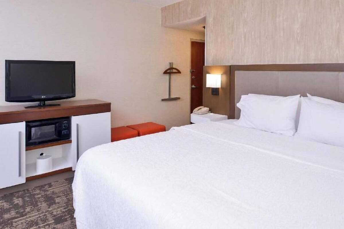 A hotel room with a bed, a television, a microwave, a telephone, and a lamp.
