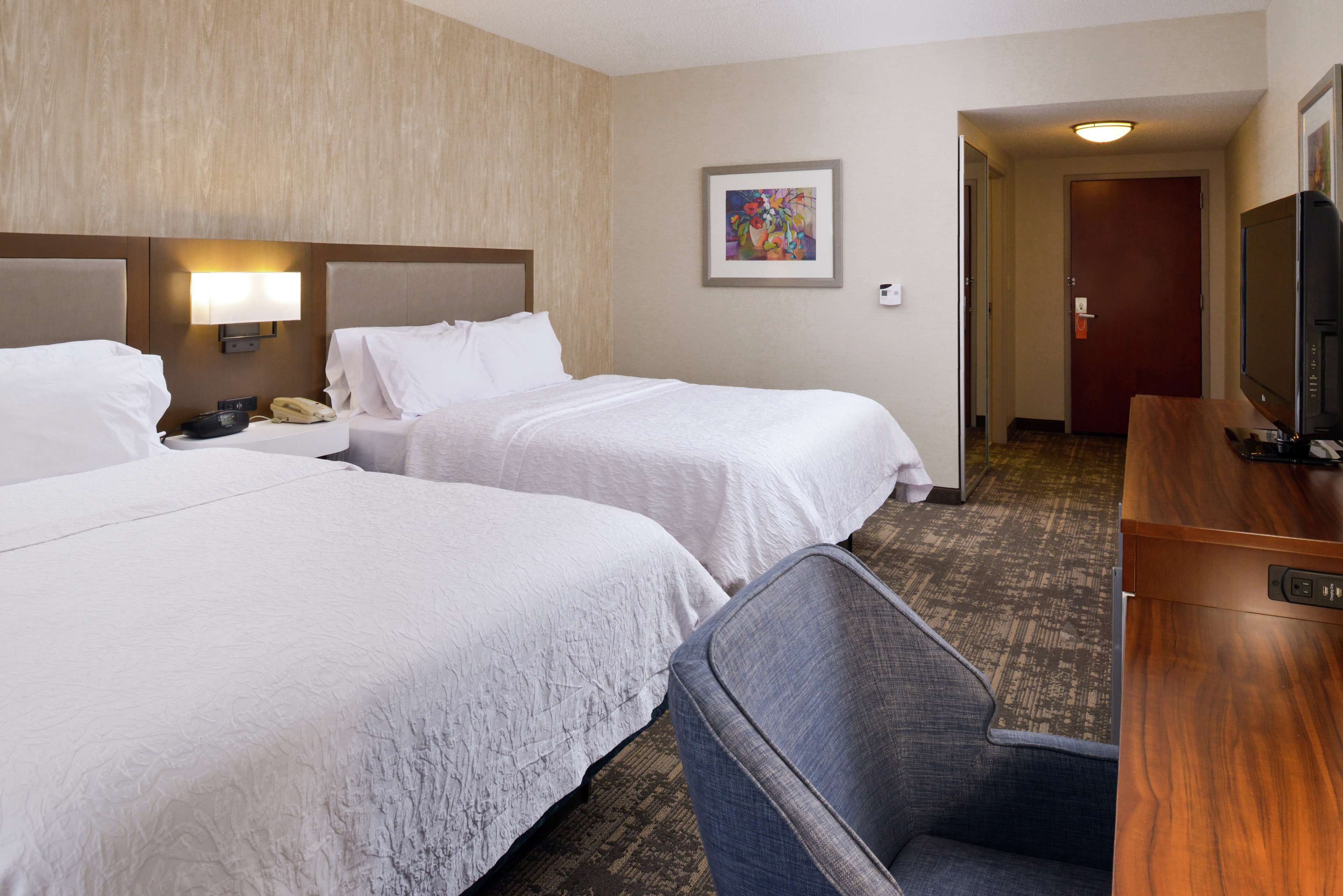 A hotel room with two beds, a desk with a television, and a chair.