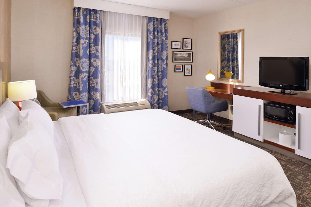 A hotel room with a large bed, a desk with a computer, a television, and a microwave.