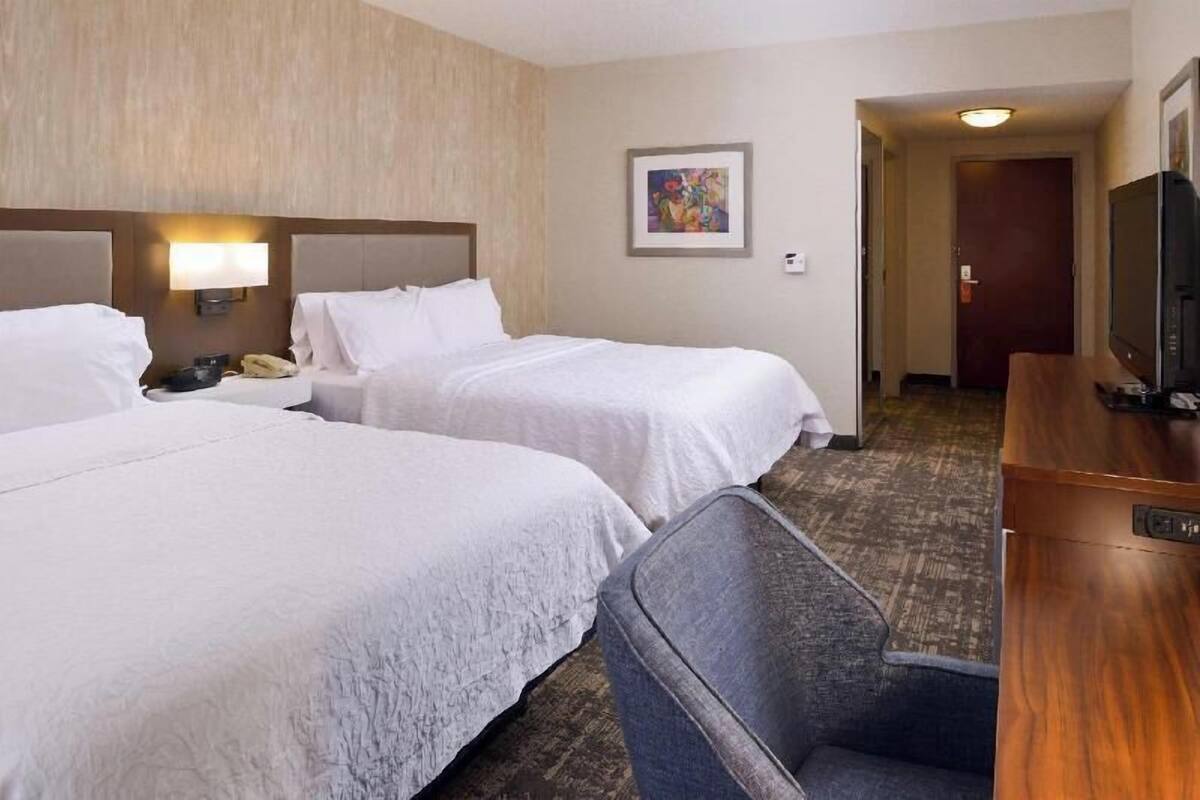 A hotel room with two beds, a desk, a chair, a television, and a painting on the wall.