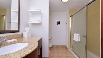 A bathroom with a granite countertop sink, a mirror, a toilet, and a glass shower enclosure.