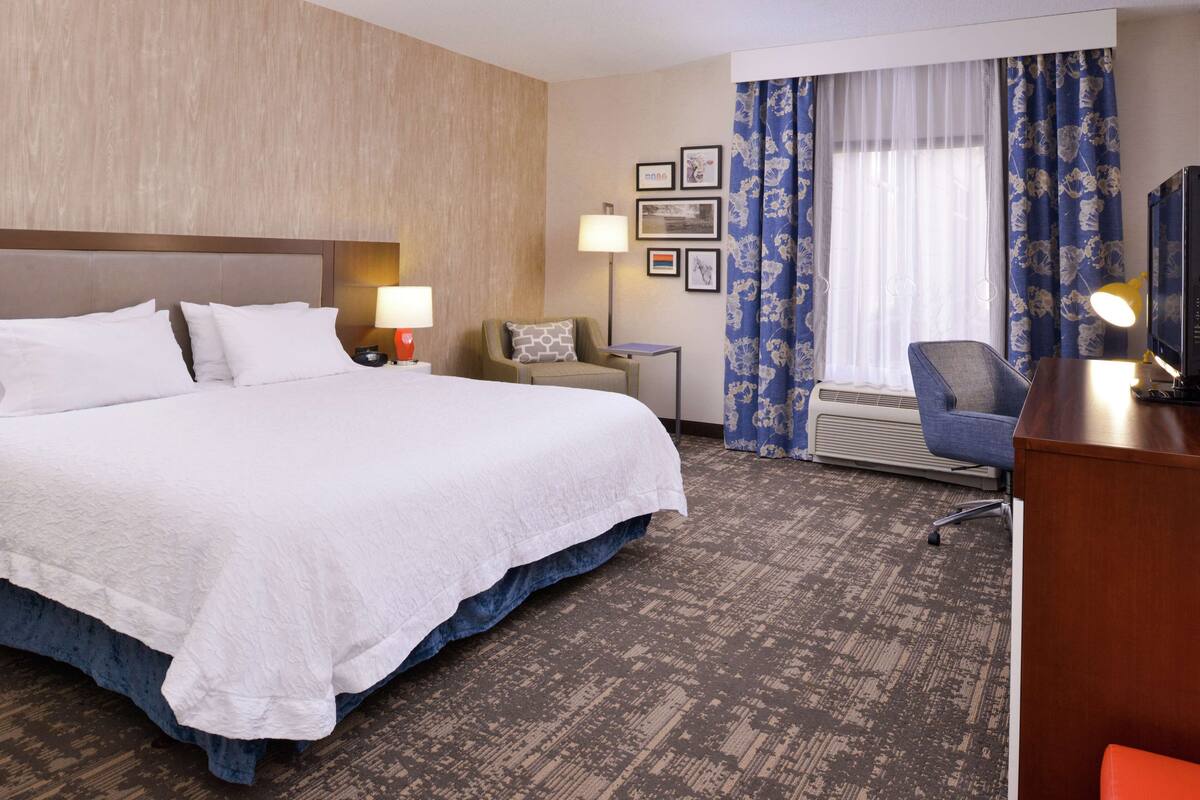 A hotel room with a large bed, a desk, a chair, and a television.