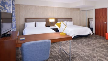 A hotel room with two beds, a desk with a chair, a TV, and a lamp.