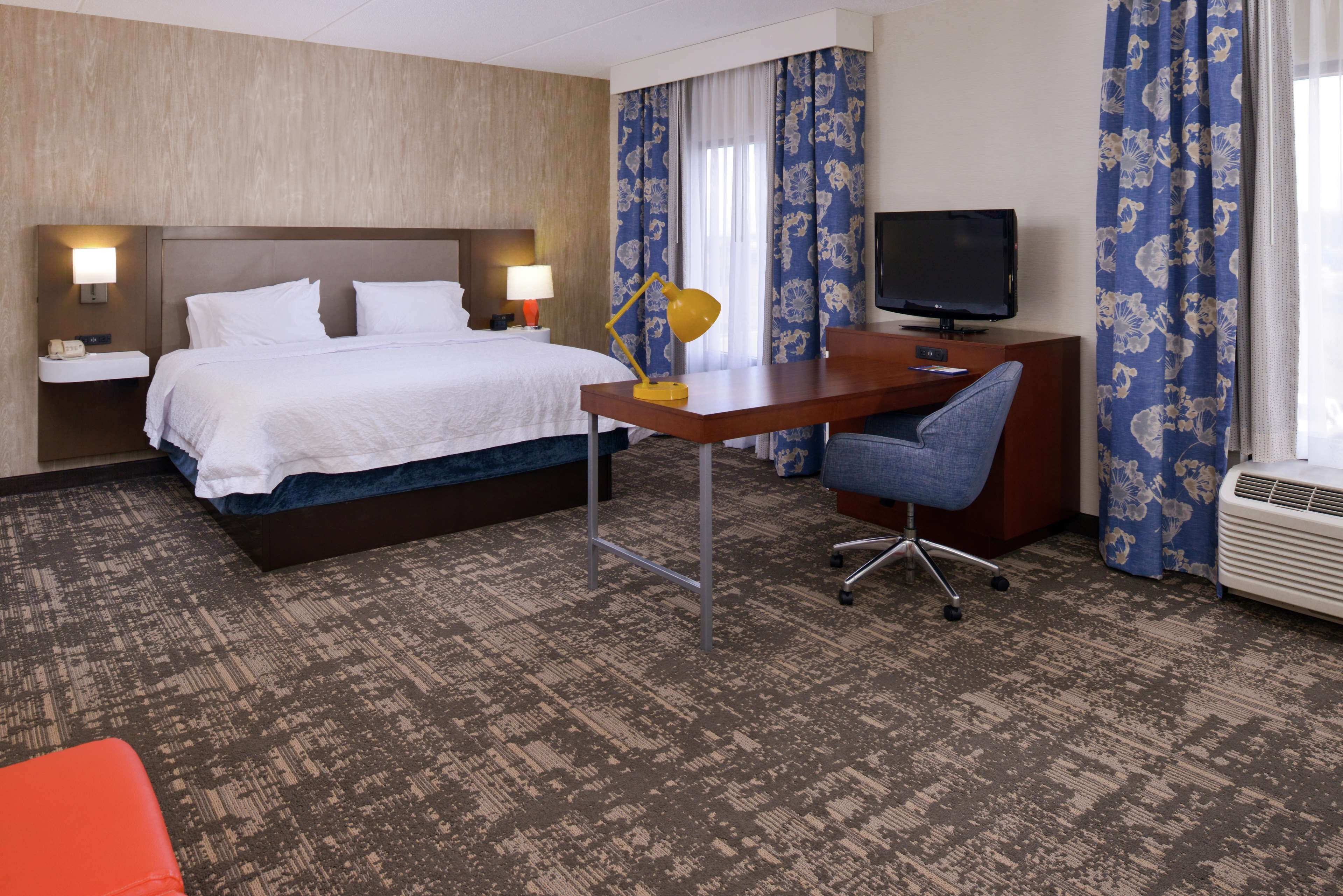 A hotel room with a bed, desk, chair, television, and air conditioning unit.