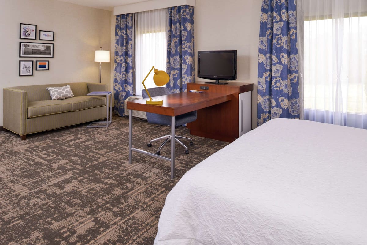 A hotel room with a bed, a desk with a computer, a chair, a sofa, a TV, and a lamp.