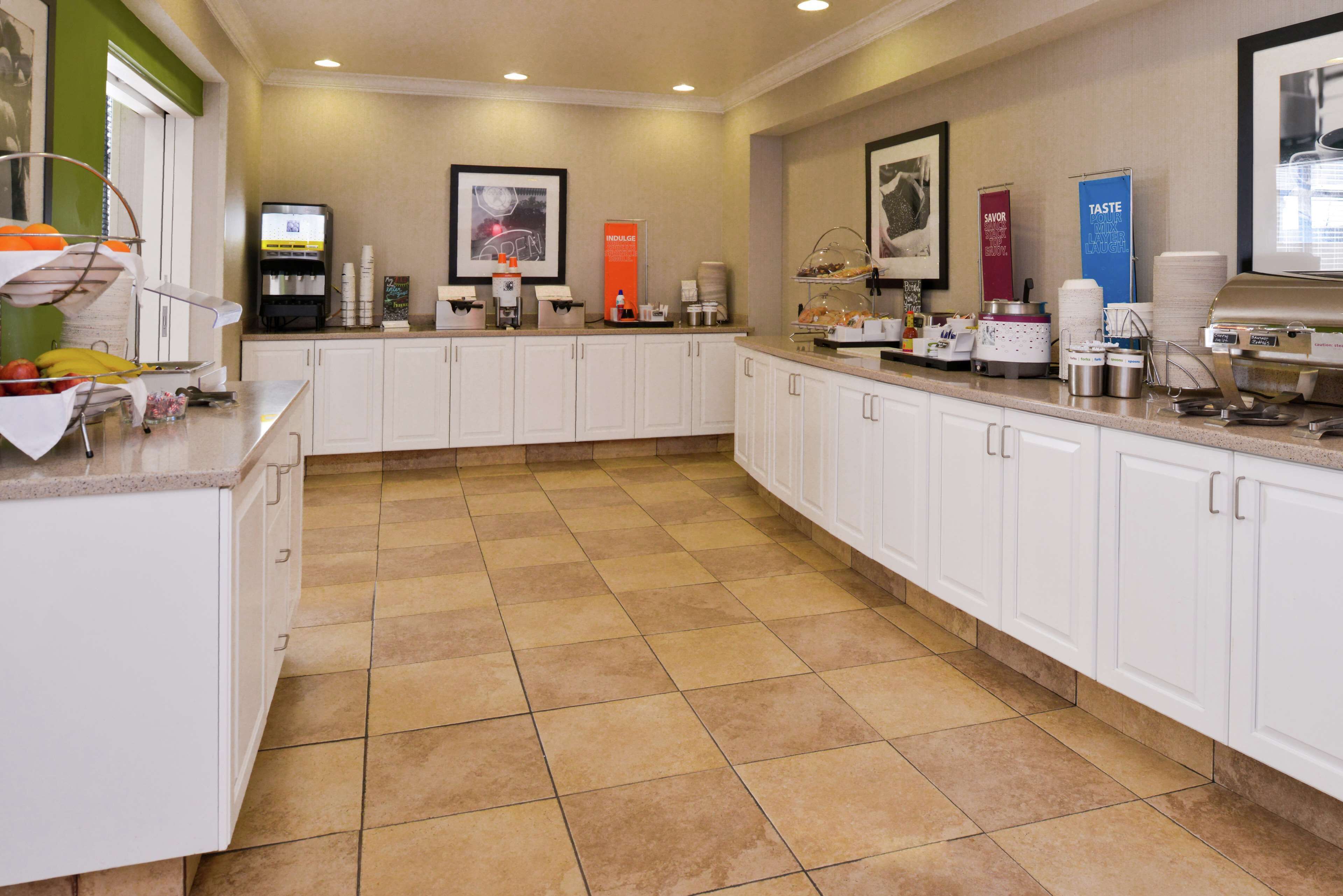 Un espace pour le petit-déjeuner à l'hôtel, avec un buffet où les clients peuvent se servir eux-mêmes, des machines à café et un distributeur d'eau fraîche.