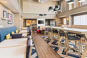 A modern hotel lobby with a long dining table, multiple seating areas, and a television mounted on the wall. - Hampton Inn & Suites Abilene I-20 (Abilene)