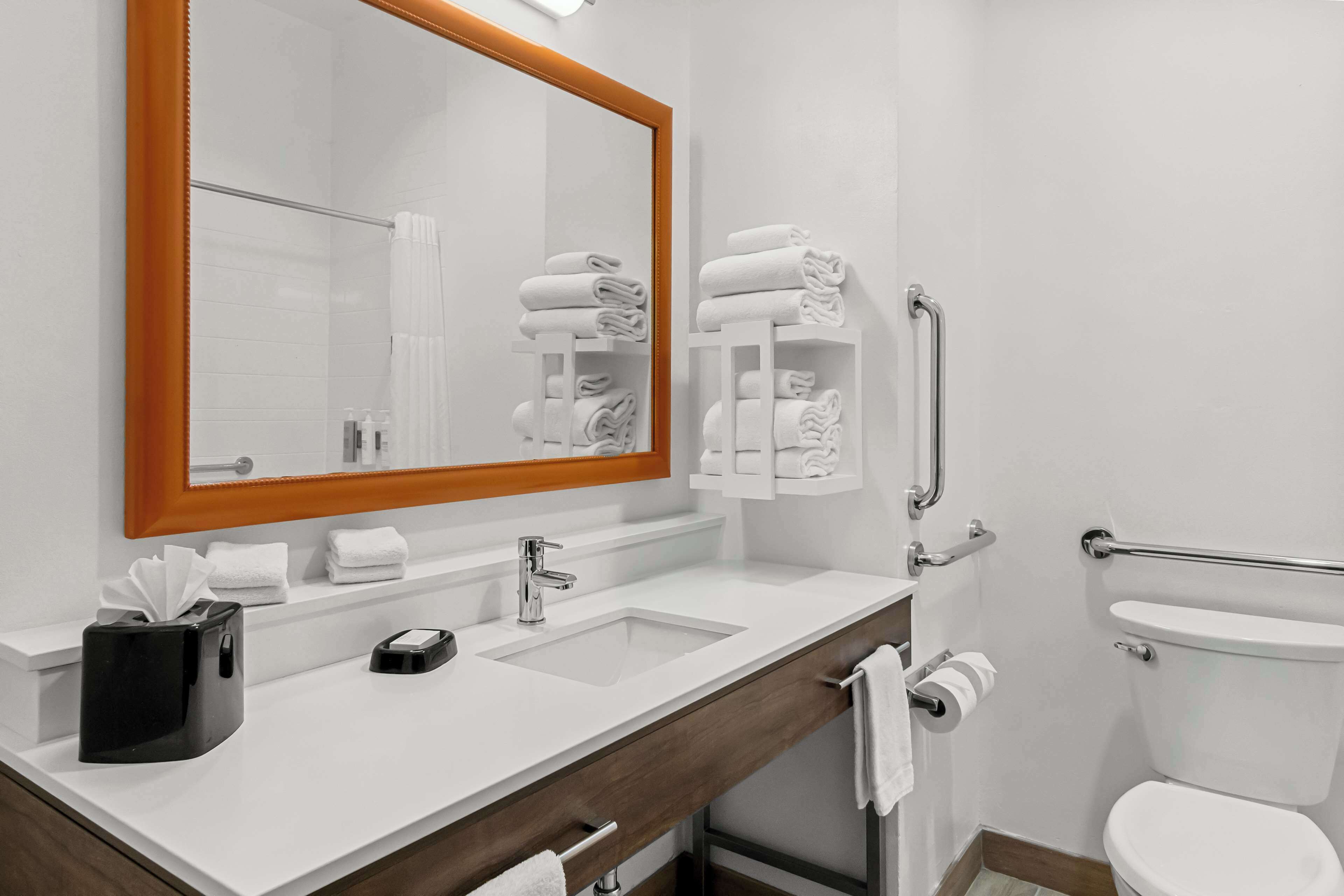 A modern bathroom with a white sink, mirror, and toilet. There are towels and toiletries on the counter.