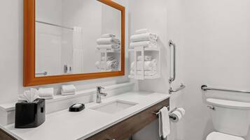 A modern bathroom with a white sink, mirror, and toilet. There are towels and toiletries on the counter.