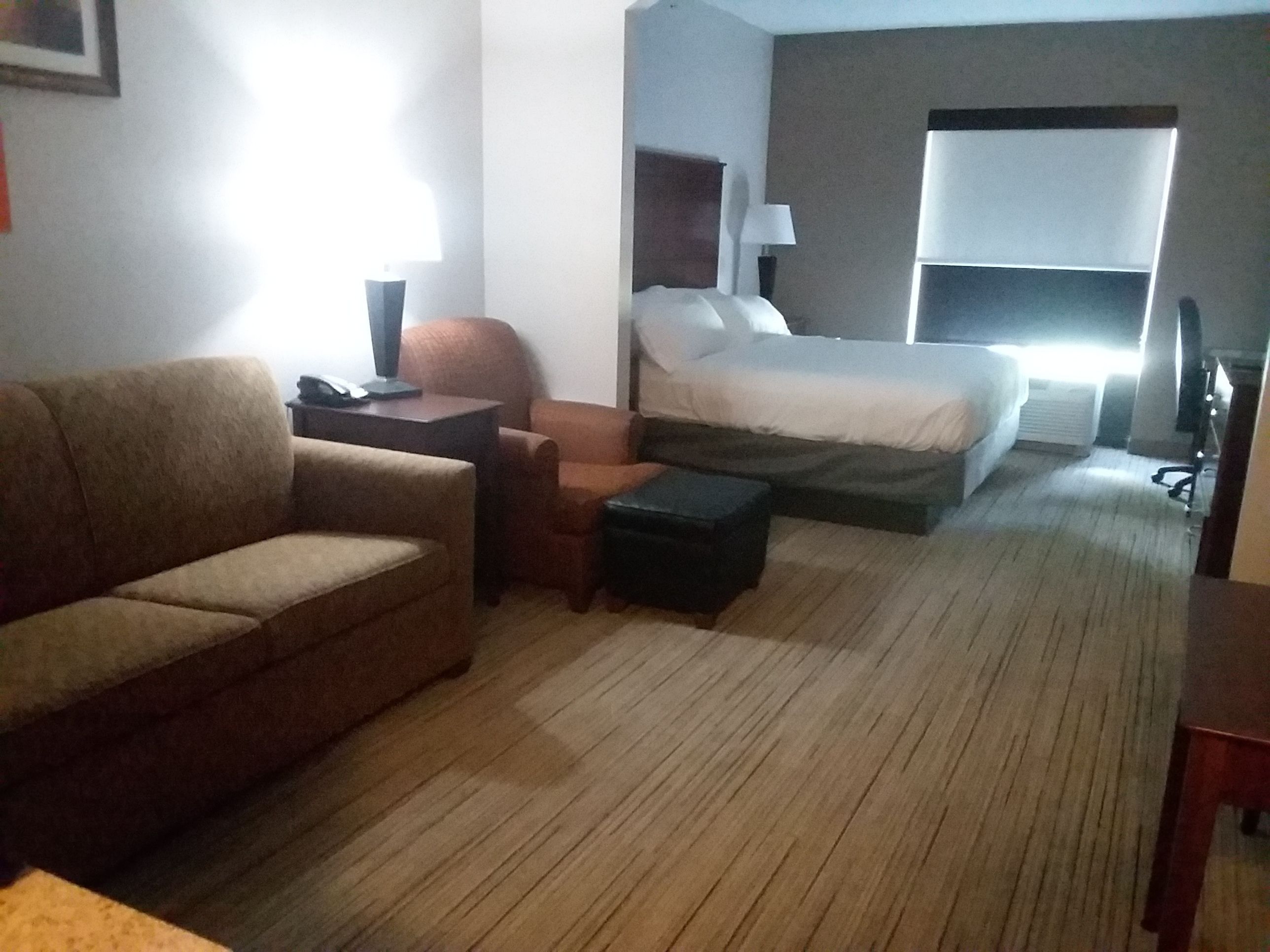 Ein Hotelzimmer mit Sofa, kleinem Tisch, Stuhl, Bett und Nachttisch.