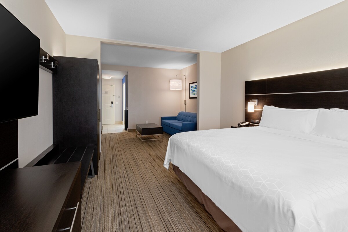 Habitación de hotel con cama, televisión, escritorio, silla y puerta que da a otra habitación.