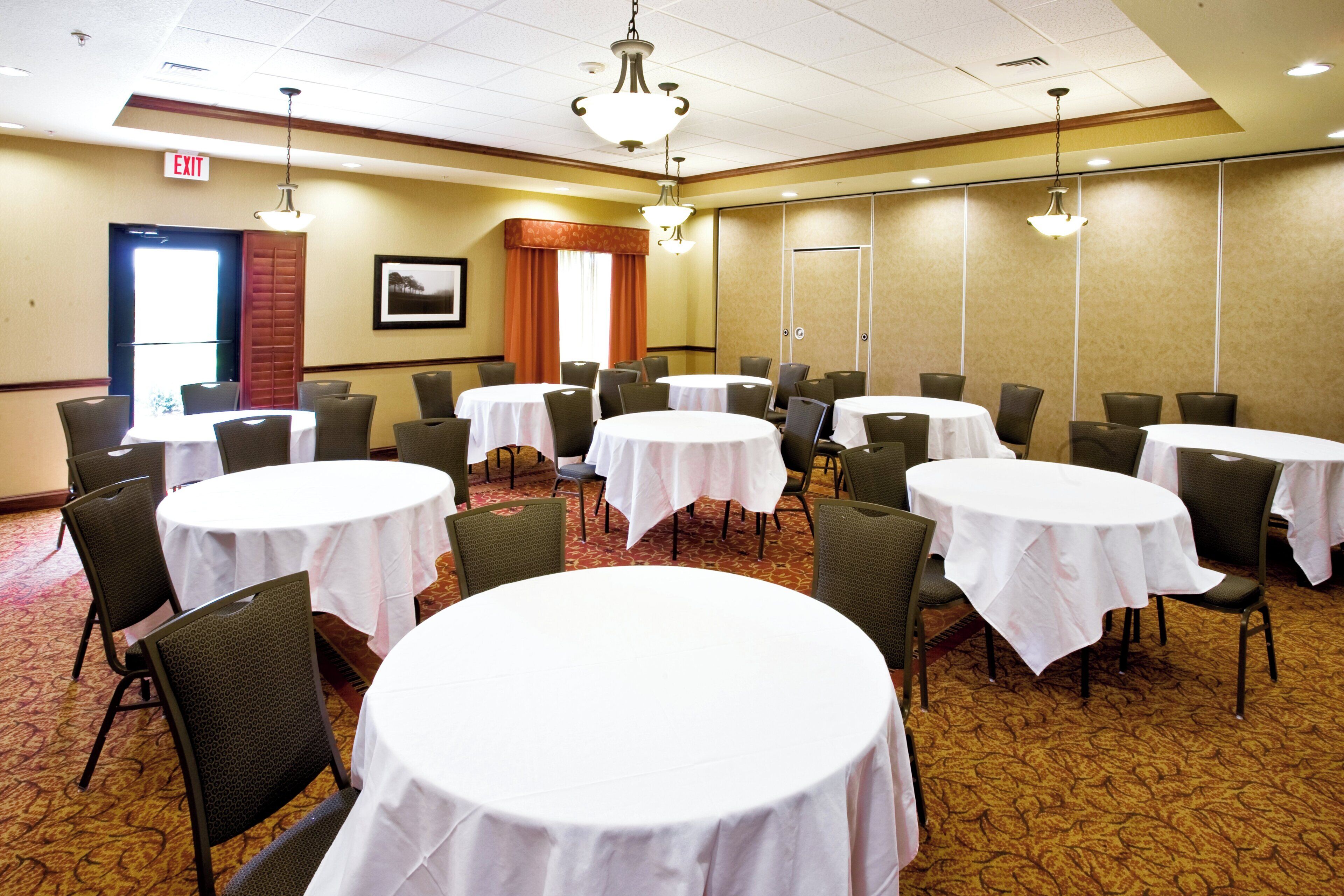 A conference room with multiple round tables, chairs, and a chandelier.