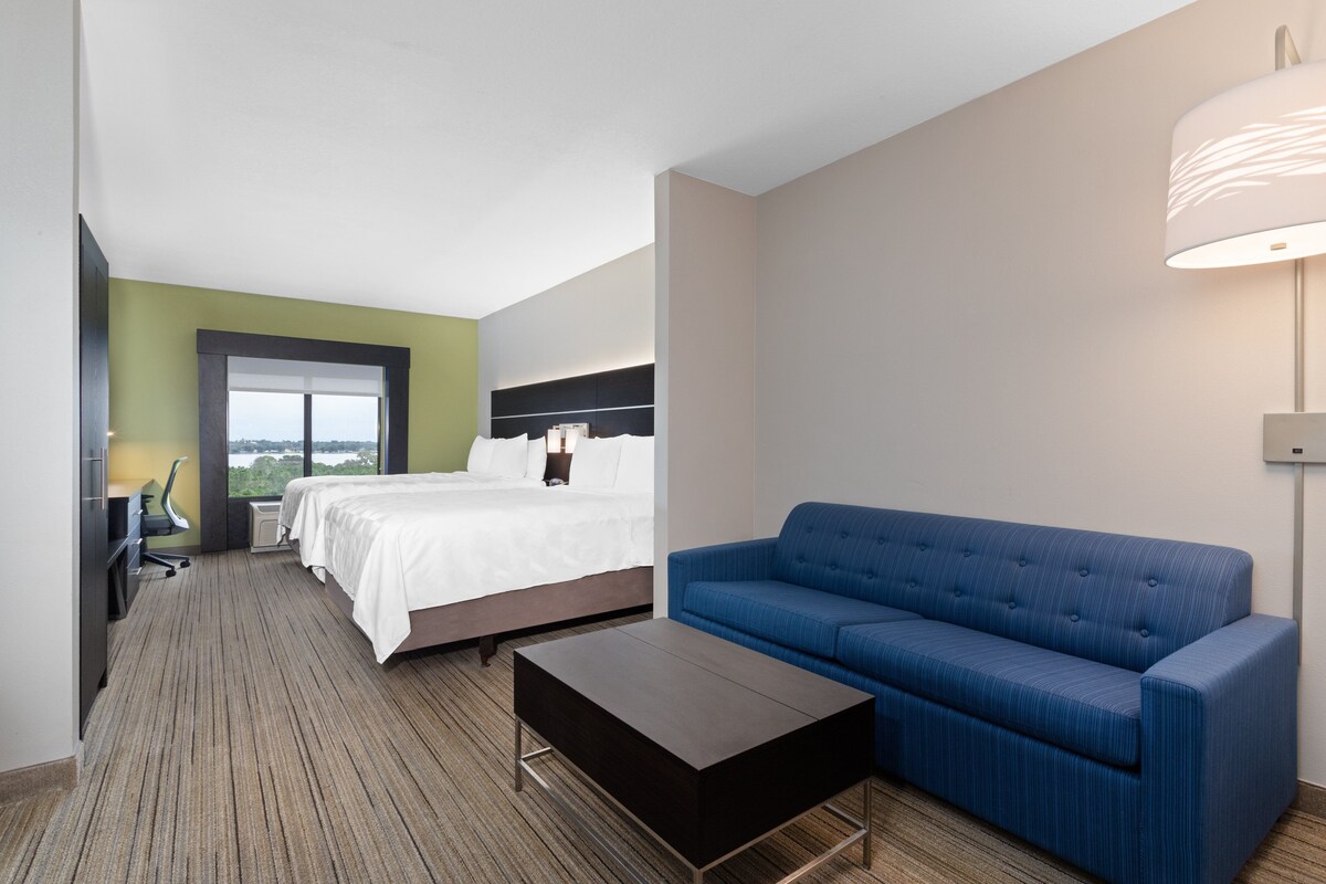 Una habitación de hotel con una cama, un sofá azul, una mesa de centro, un escritorio con una silla y un ventanal grande.