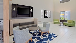 A modern lobby with a sofa, chairs, a TV, framed pictures, and a large window.