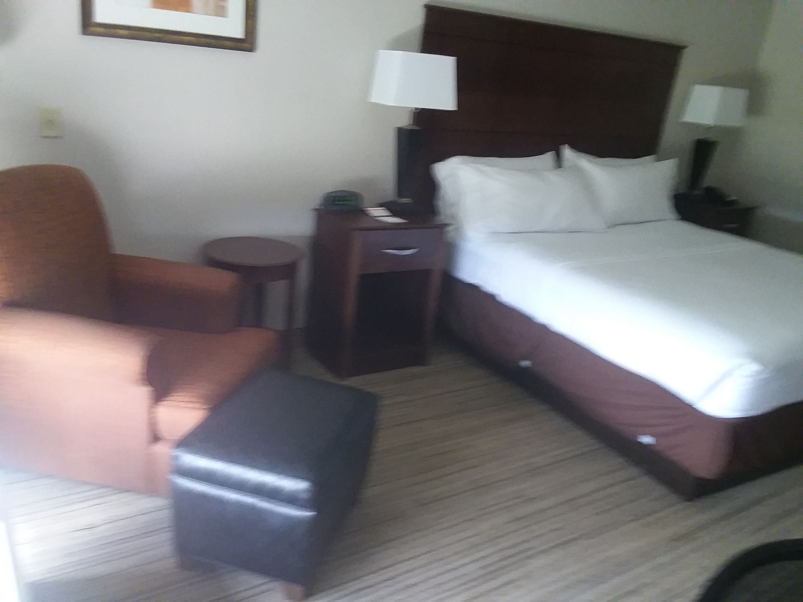 A hotel room with a bed, a chair, a small table, and a nightstand.