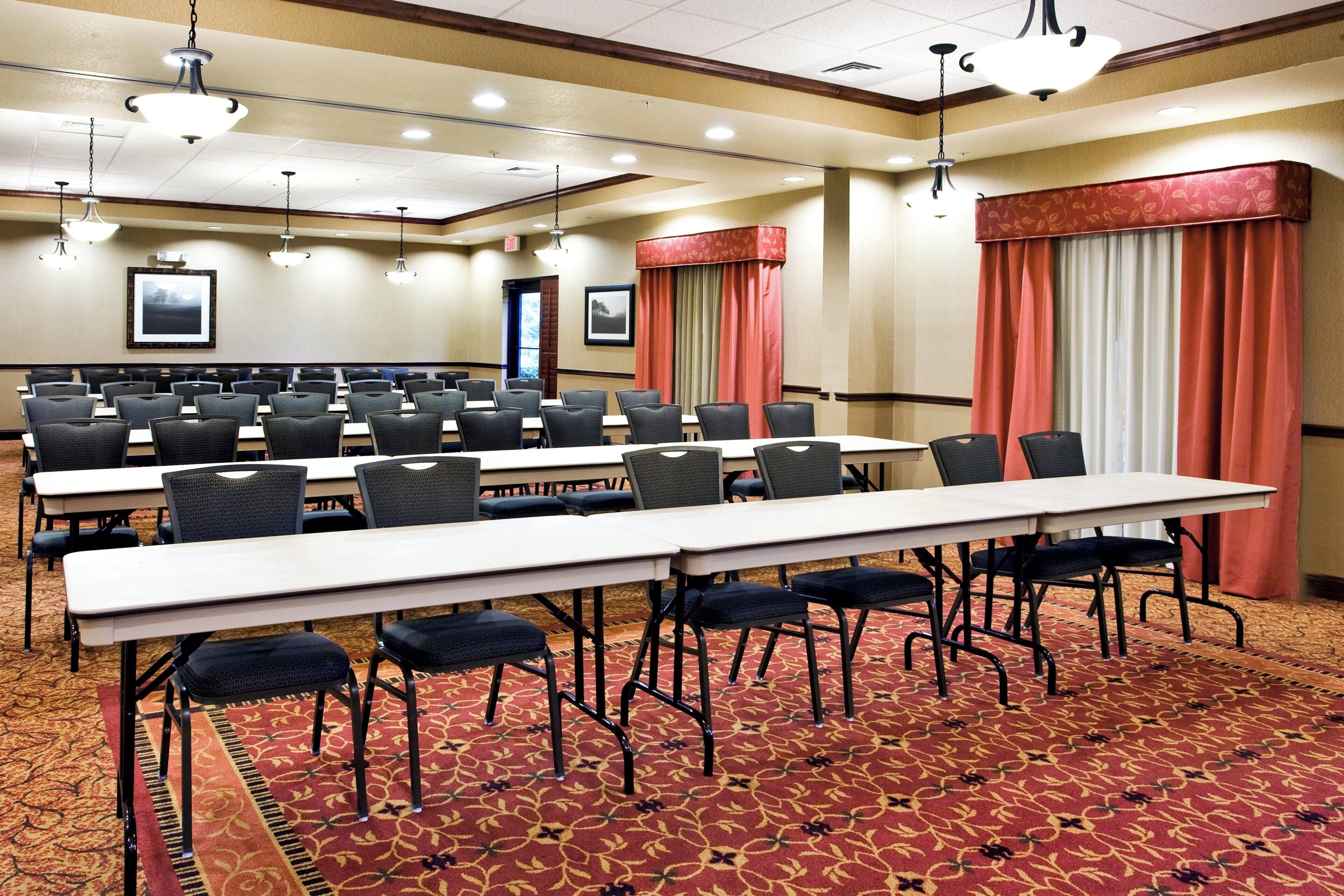 A conference room with multiple tables and chairs, carpeted flooring, and ceiling lights.