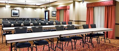 A conference room with multiple tables and chairs, carpeted flooring, and ceiling lights.