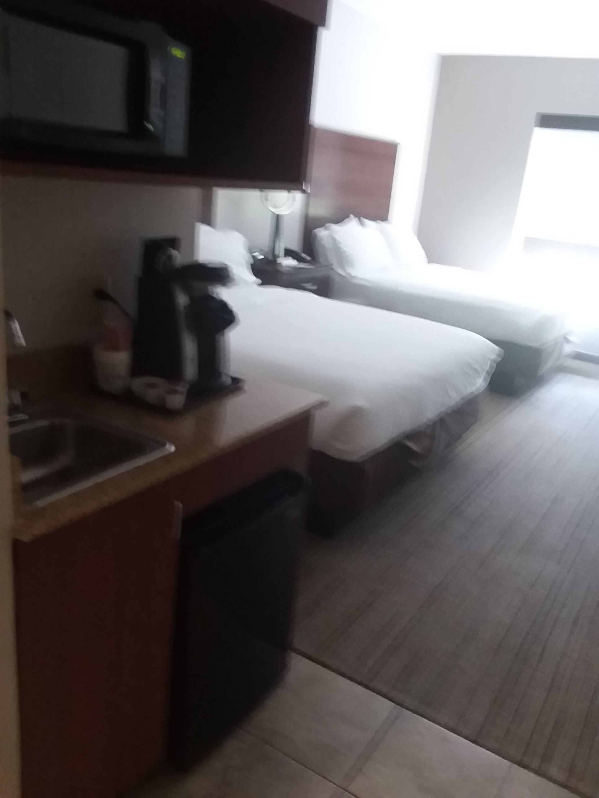 Quarto de hotel com cozinha compacta, cama, mesa de cabeceira e janela.