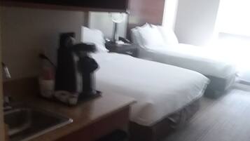Quarto de hotel com cozinha compacta, cama, mesa de cabeceira e janela.