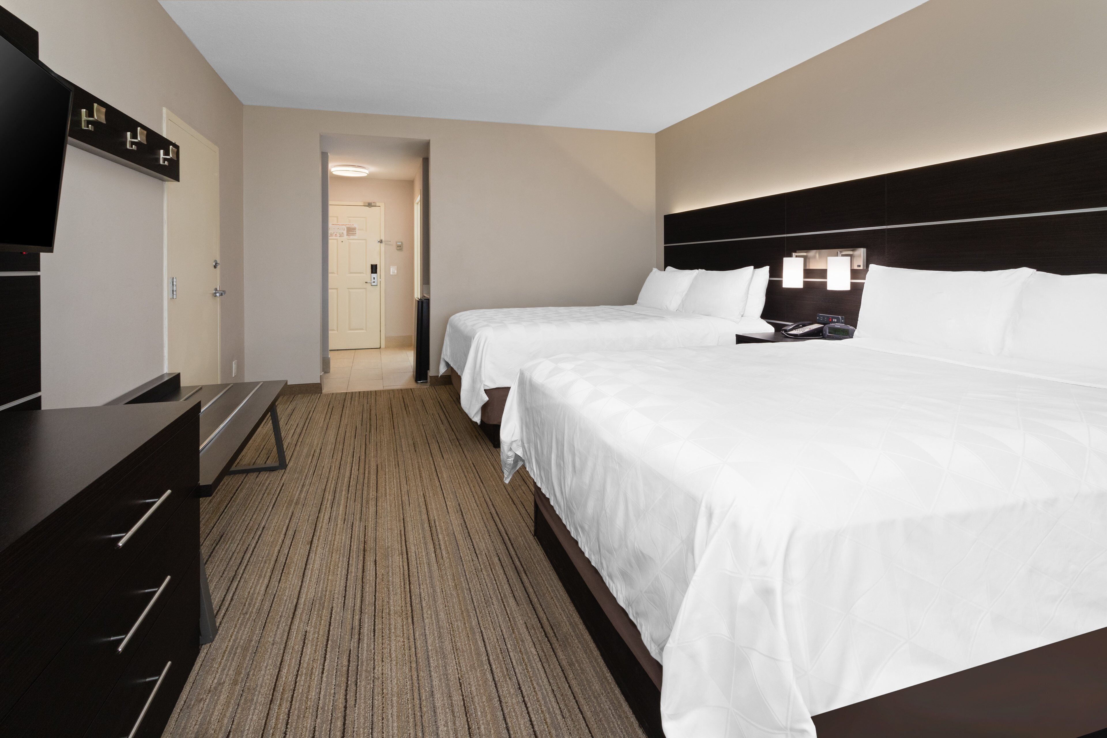 Une chambre d’hôtel avec un grand lit, une télévision, un bureau et un sol recouvert de moquette.