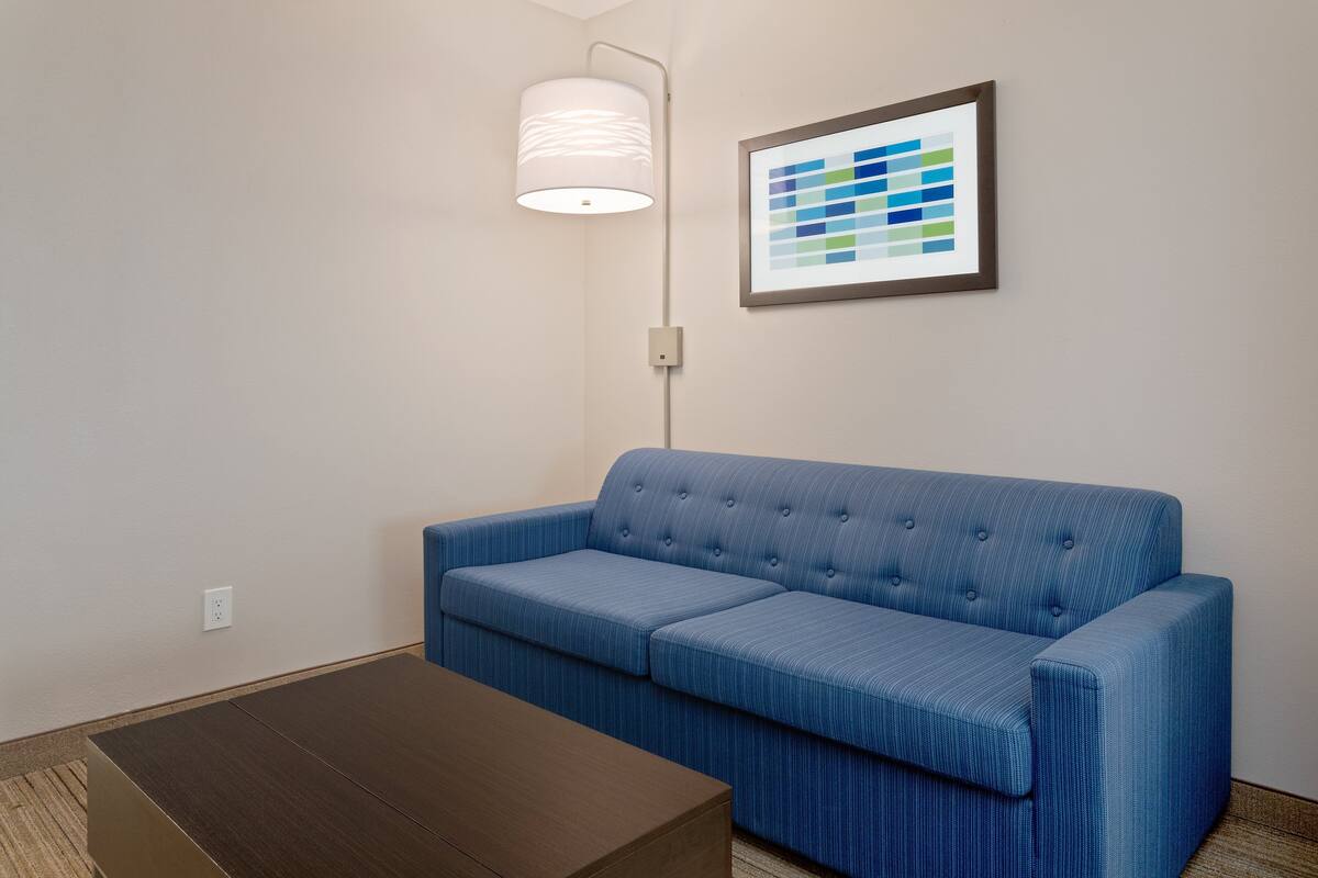Una habitación con un sofá azul, una mesa de centro de madera, una lámpara de pared y una obra de arte abstracta enmarcada.