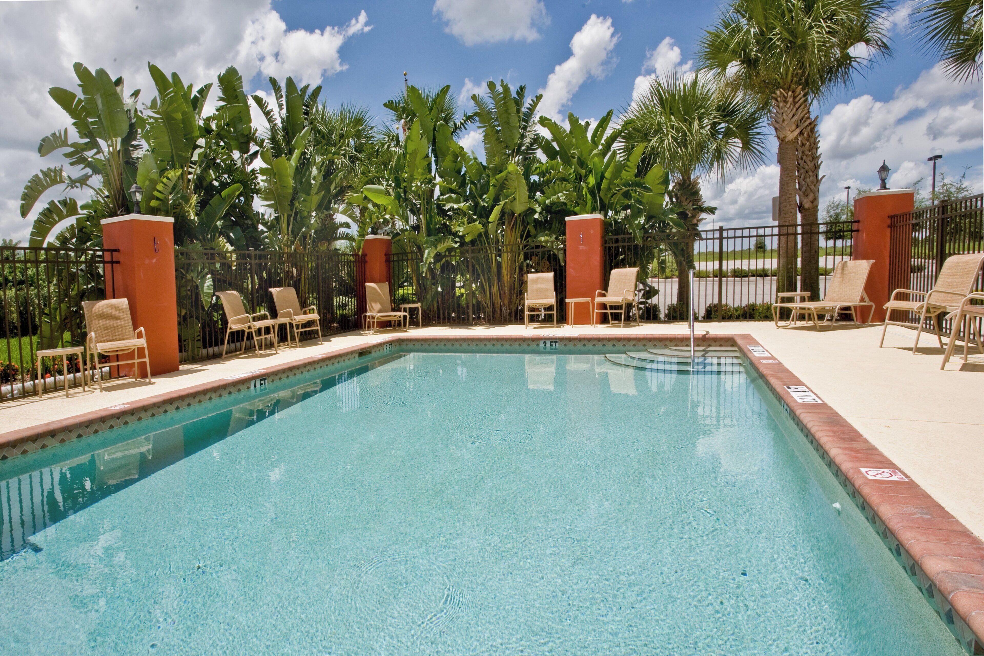 A clear blue pool surrounded by lounge chairs and palm trees.