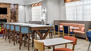 A modern hotel lobby with a long dining table, multiple chairs, a sofa, and a fireplace. - Hampton Inn & Suites Farmington (Farmington)