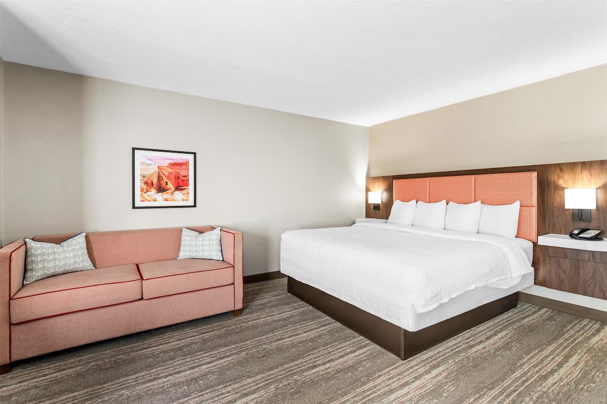 Una habitación de hotel con una cama, un sofá, una mesita de noche y una lámpara fijada a la pared.