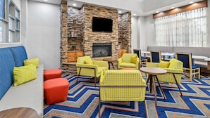 A lobby with a stone wall, a fireplace, yellow and blue furniture, and a patterned carpet. - Hampton Inn & Suites Farmington (Farmington)