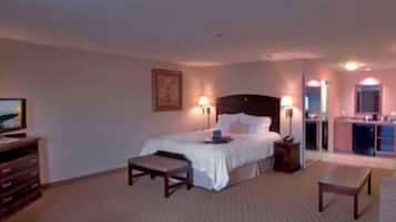 A hotel room with a bed, bedside tables, a desk, a chair, a dresser, and a television.