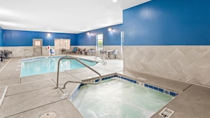 An indoor swimming pool with a blue and beige tiled floor, a seating area with chairs and tables, and a clear view of the pool's edge. - Hampton Inn & Suites Farmington (Farmington)