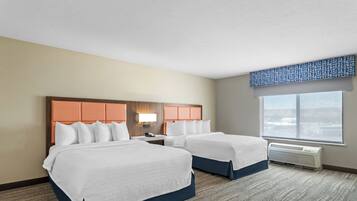 A hotel room with two beds, a large window, and a wall-mounted air conditioner.