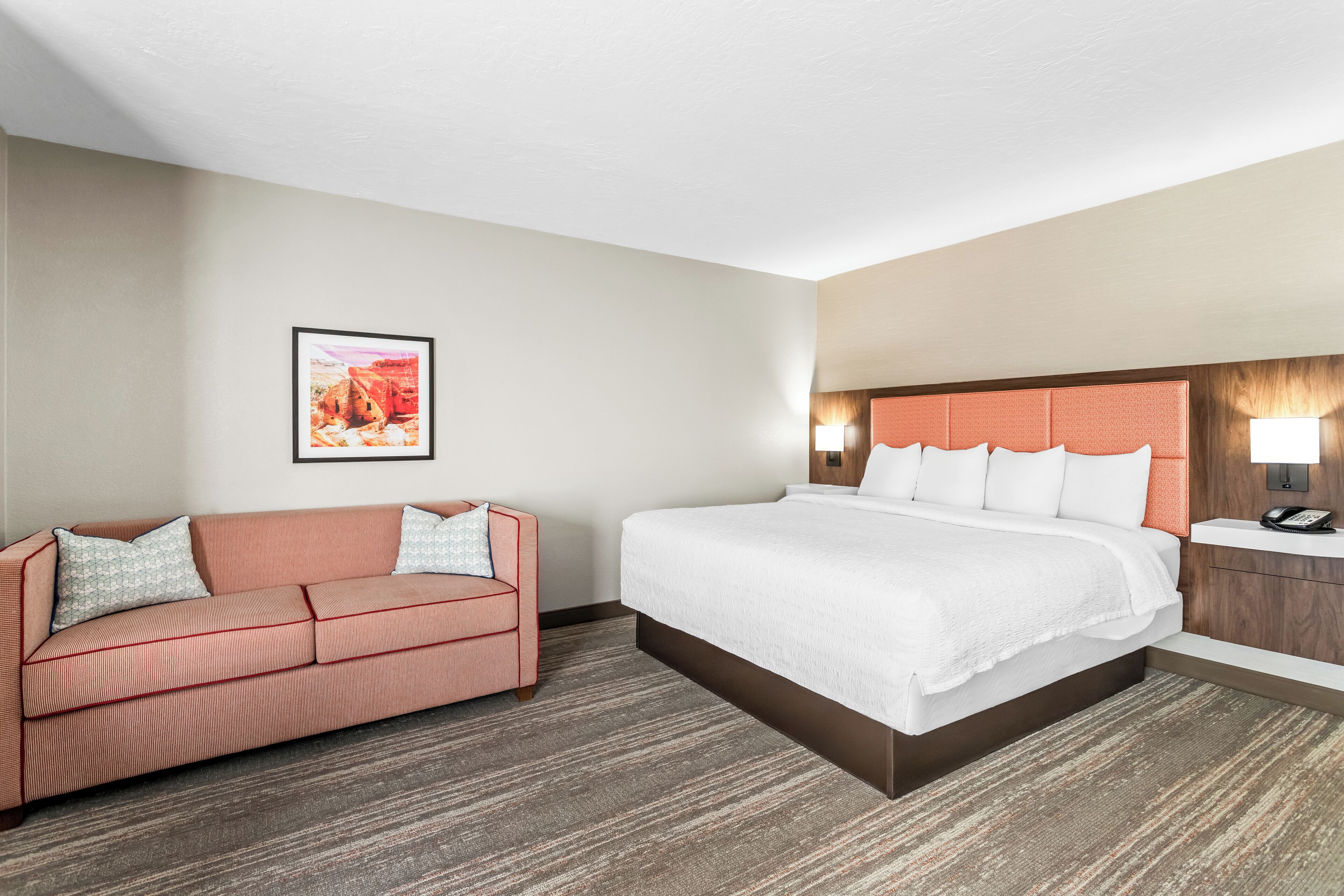 A hotel room with a large bed, a sofa, a nightstand, and a wall-mounted lamp.