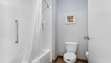 Et badeværelse med bruser, toilet og et billede i ramme på væggen.