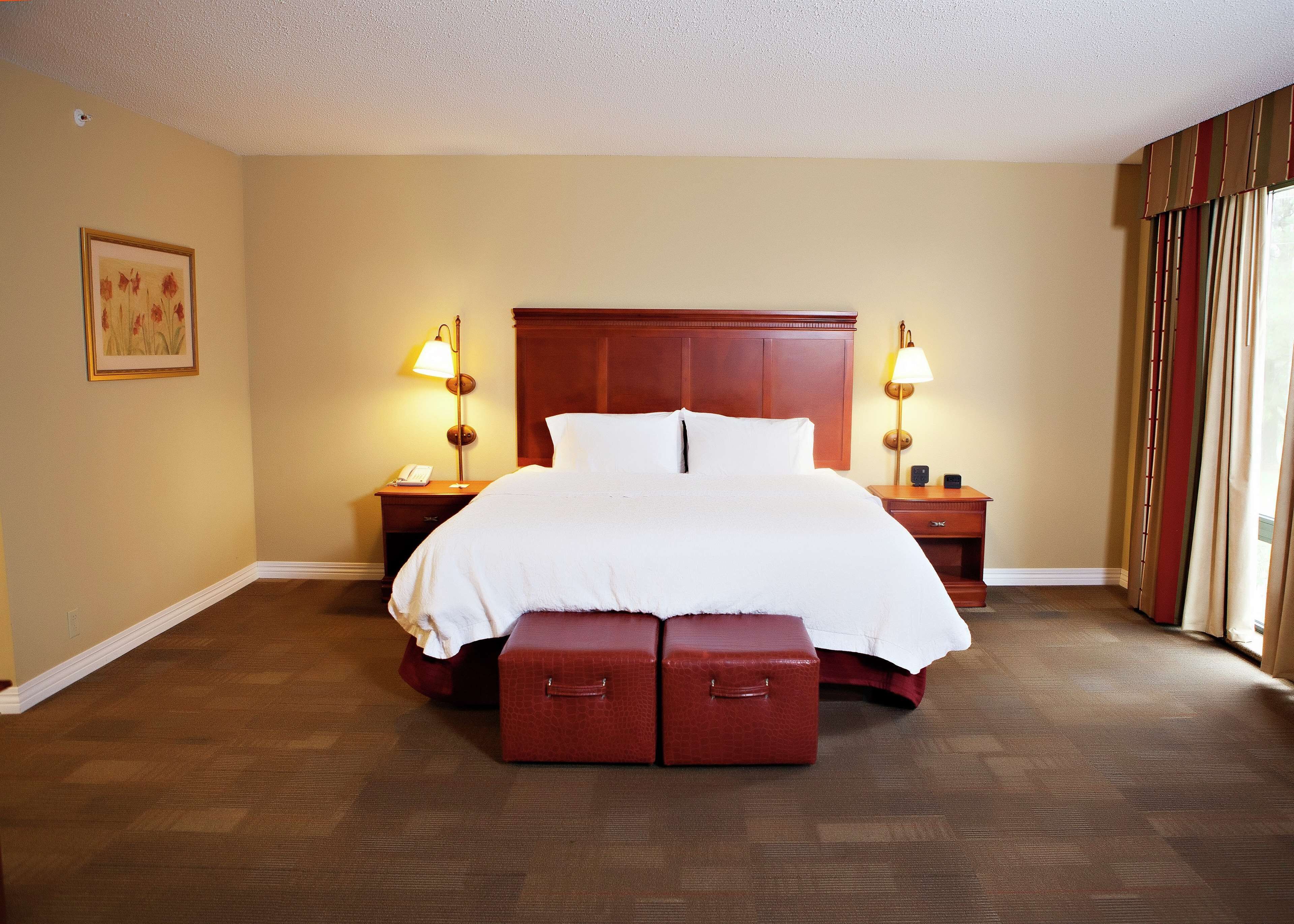 A hotel room with a large bed, two bedside tables with lamps, a framed picture on the wall, and a window with curtains.