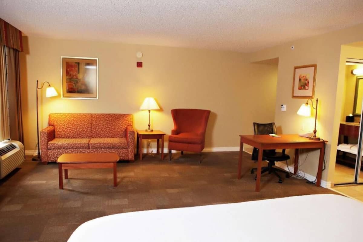 A hotel room with a bed, a sofa, a chair, a table, and two lamps.