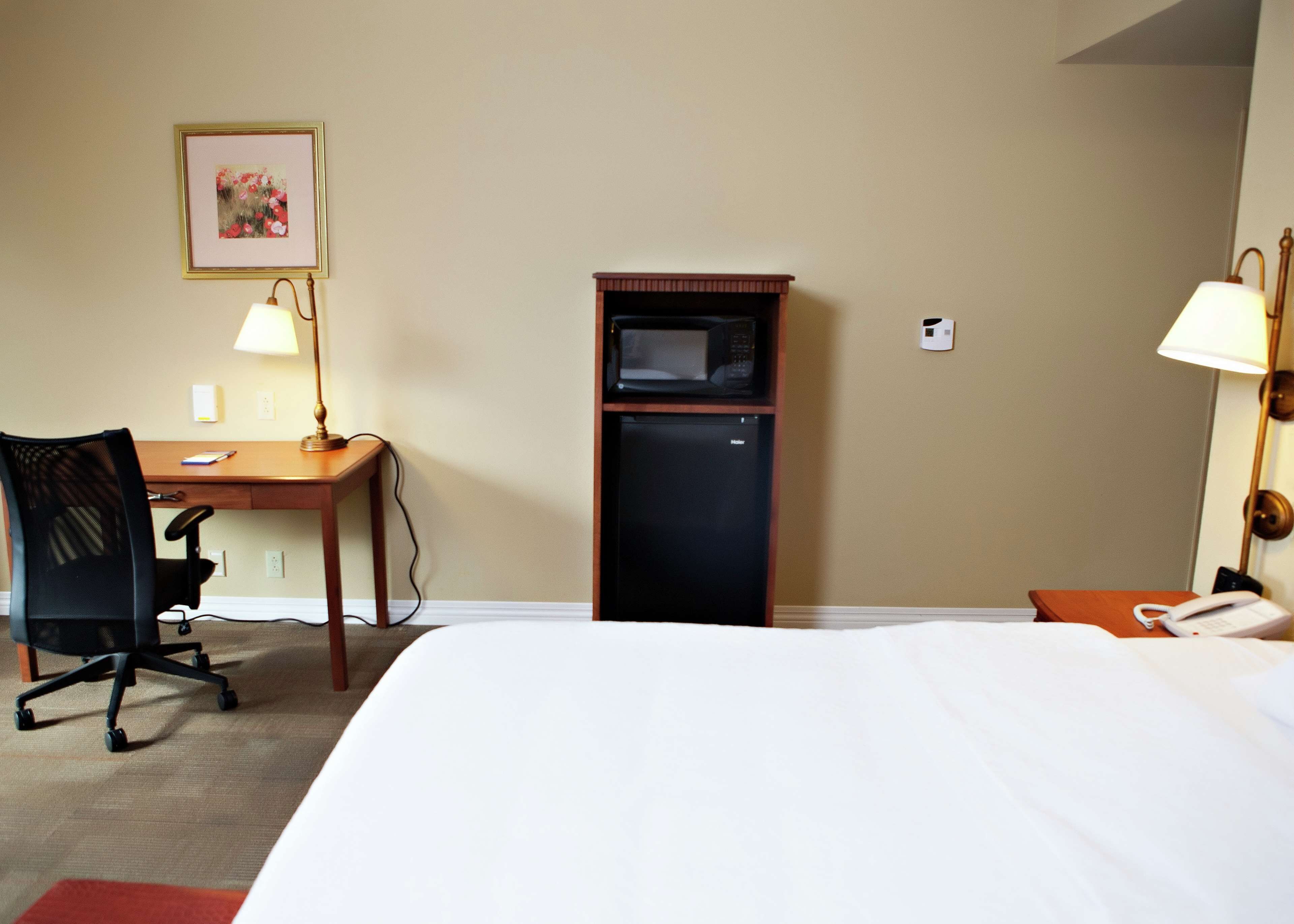 A hotel room with a bed, desk, chair, microwave, and telephone.
