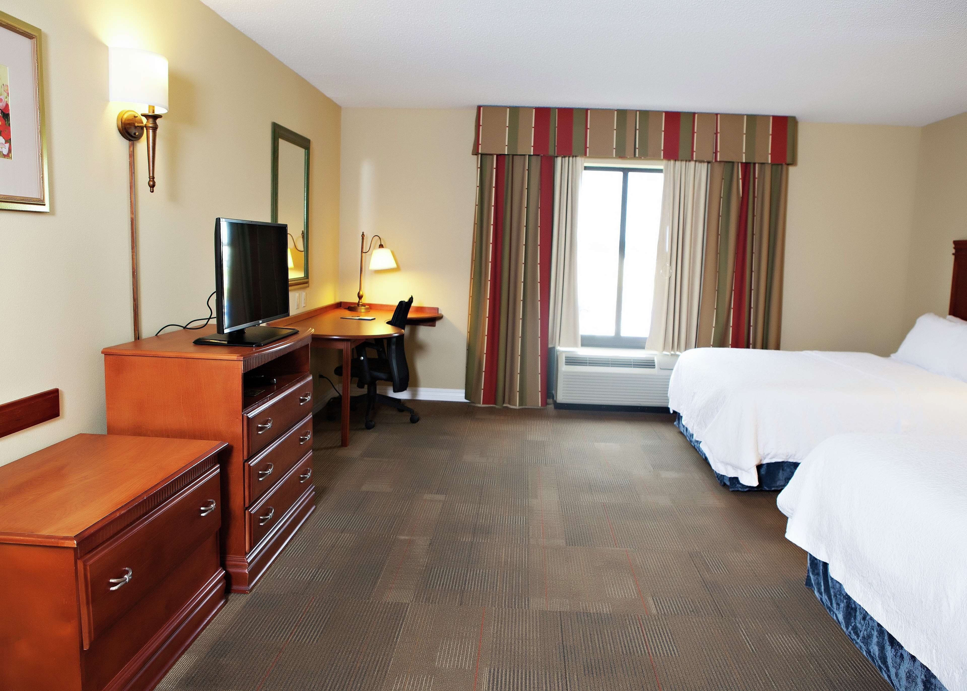Una habitación de hotel con escritorio, silla, televisor, cómoda y dos camas.