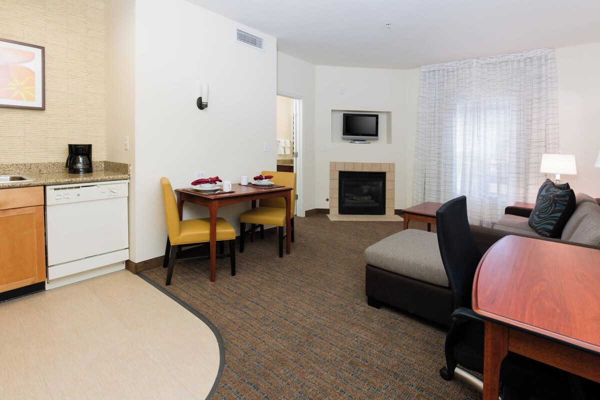 A hotel room with a kitchenette, a dining area with a table and chairs, a living area with a sofa and a TV, and a fireplace.