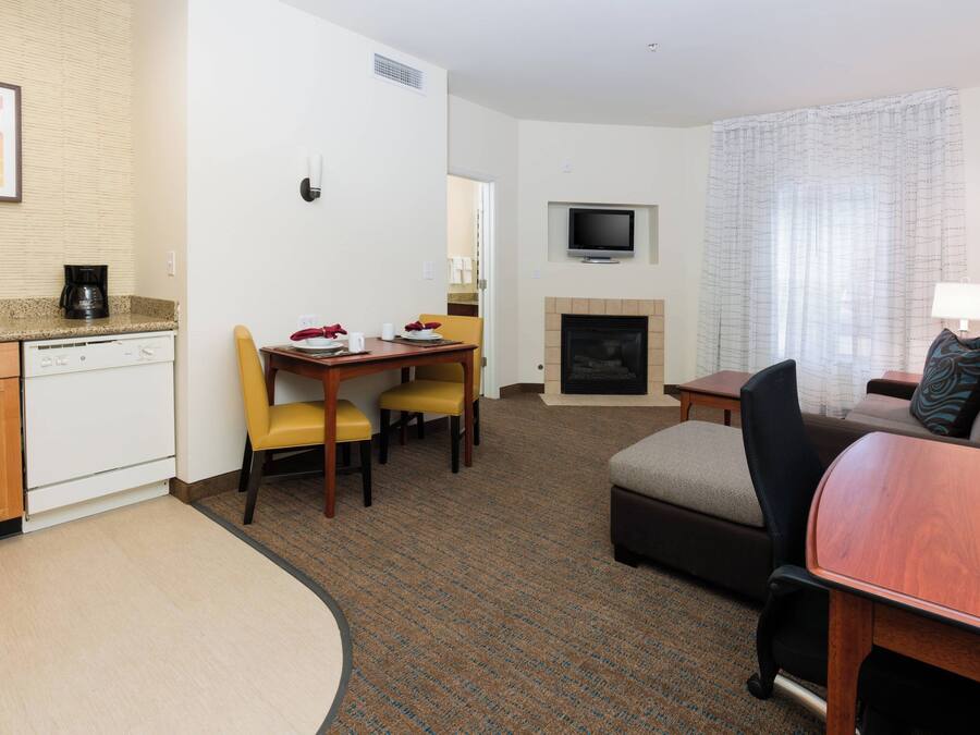 Quarto de hotel com cozinha compacta, área de refeições com mesa e cadeiras, sala de estar com sofá e televisão, e lareira.