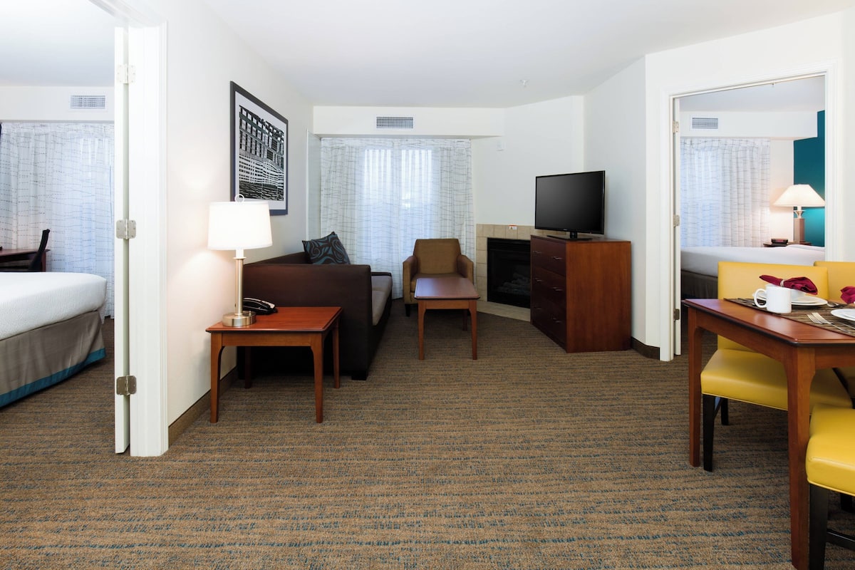 A hotel room with a bed, a sofa, a desk, a television, and a dining area.