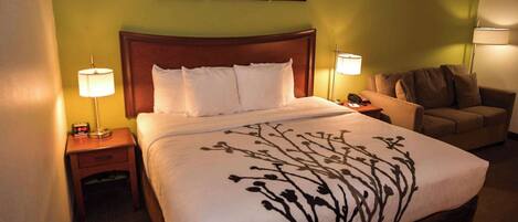 A hotel room with a large bed, a nightstand with a lamp, a chair, and framed pictures on the wall.