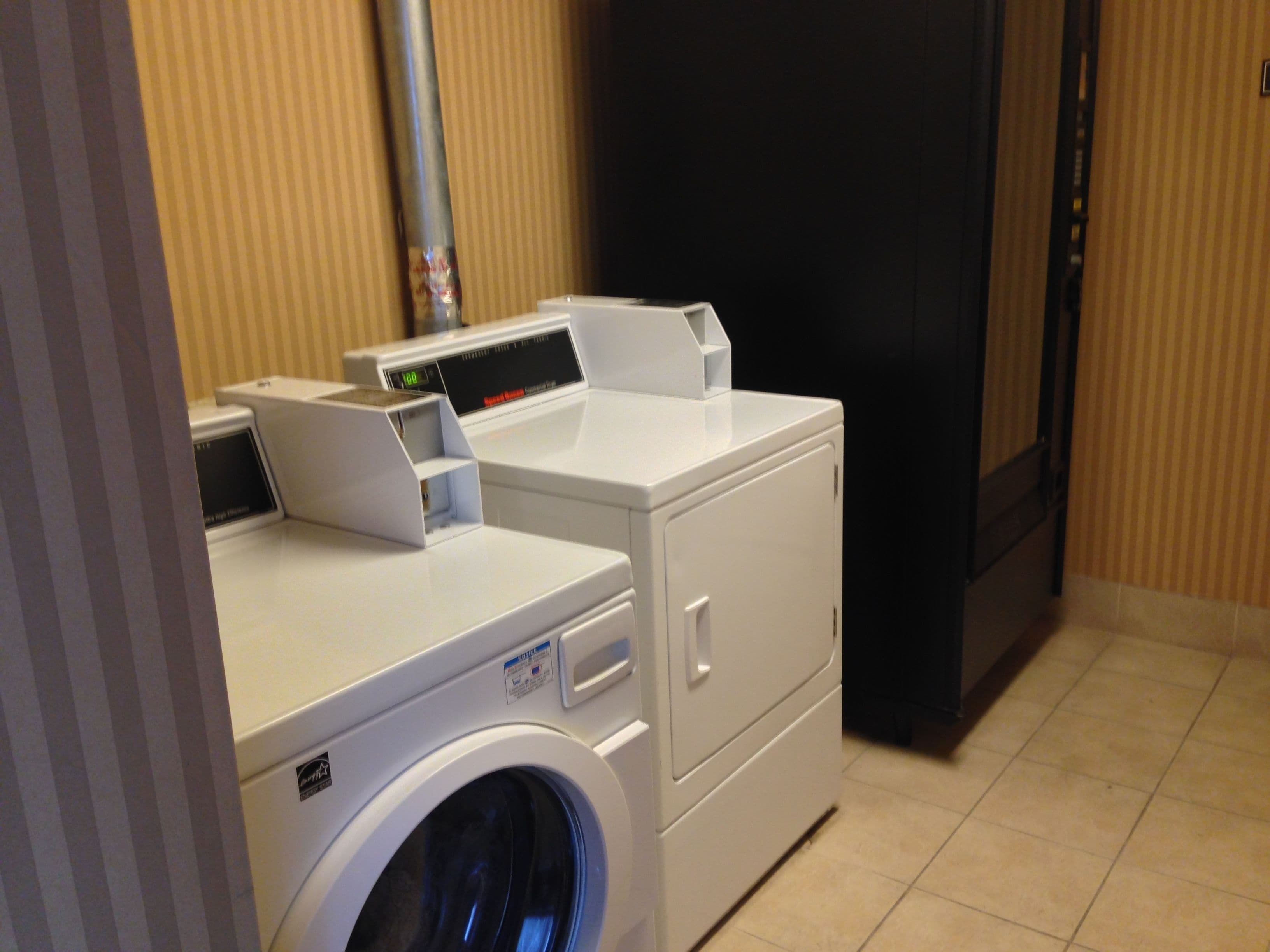 A laundry room with a front-loading washer and dryer, a control panel, and a black refrigerator.