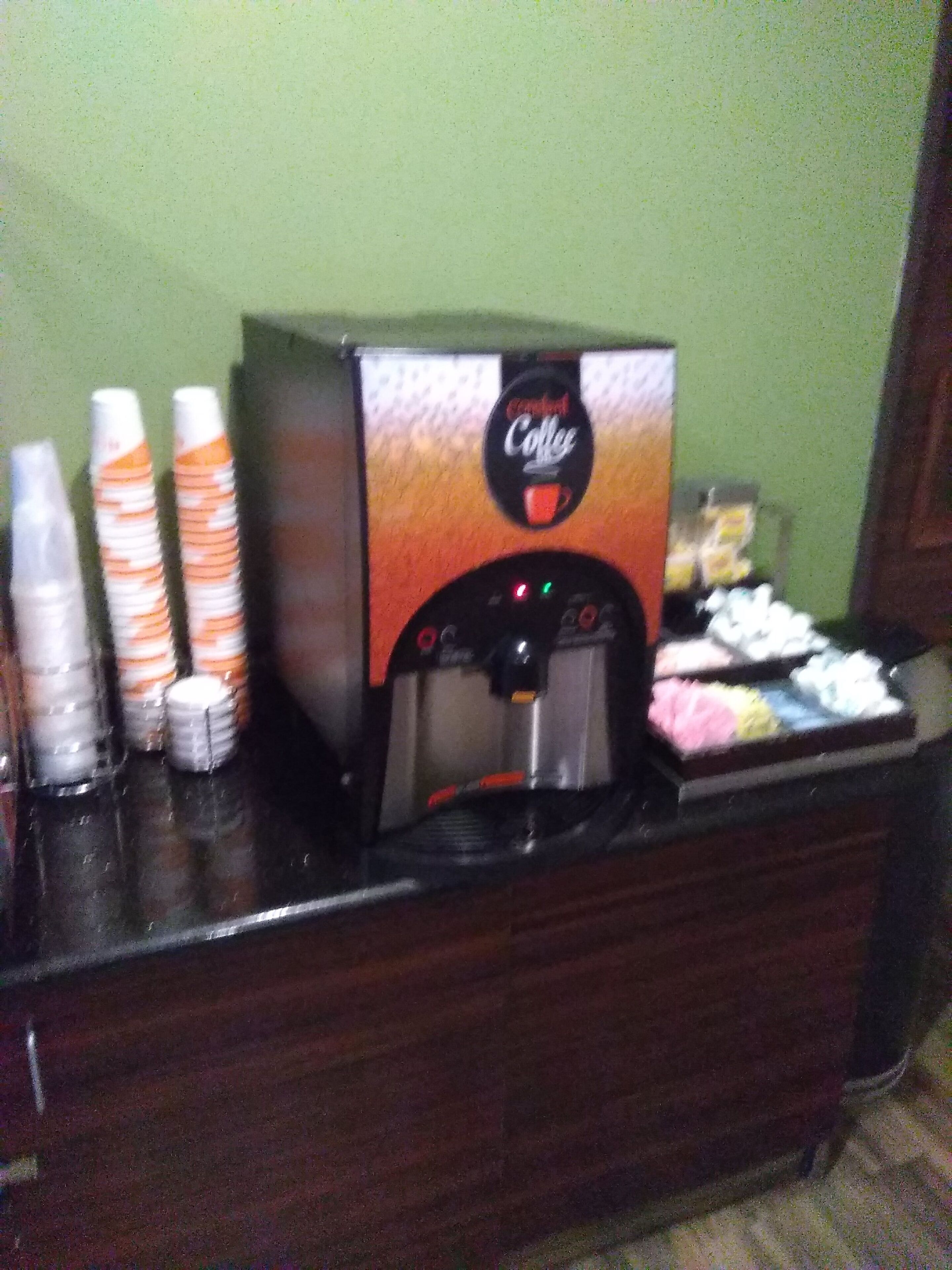Een koffieapparaat met wegwerpbekers en een bak met snacks op een toonbank.