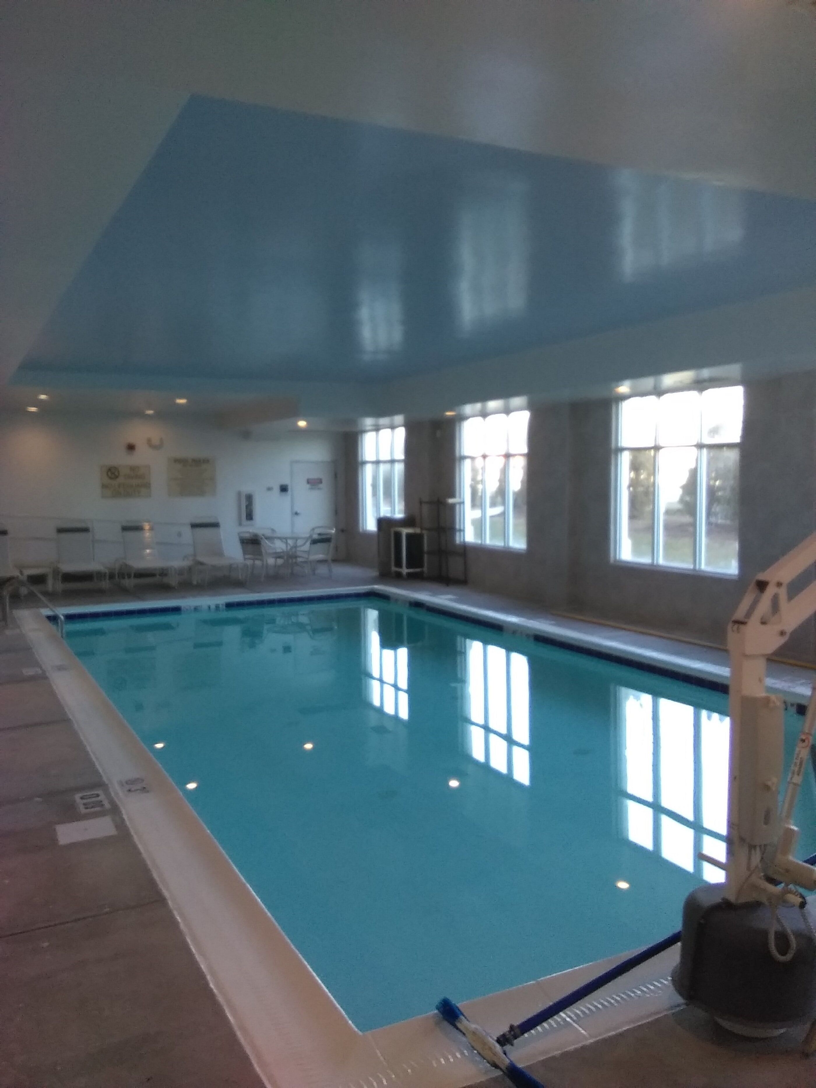 Une piscine intérieure à l’eau claire, entourée de murs et de fenêtres.