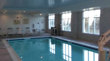 Une piscine intérieure à l’eau claire, entourée de murs et de fenêtres.