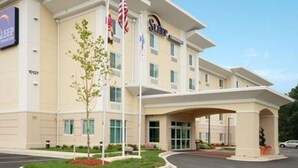 A hotel with a modern design, featuring a central entrance with a covered walkway, multiple windows, and a flagpole with flags. - Sleep Inn & Suites Laurel near Fort Meade (Laurel)